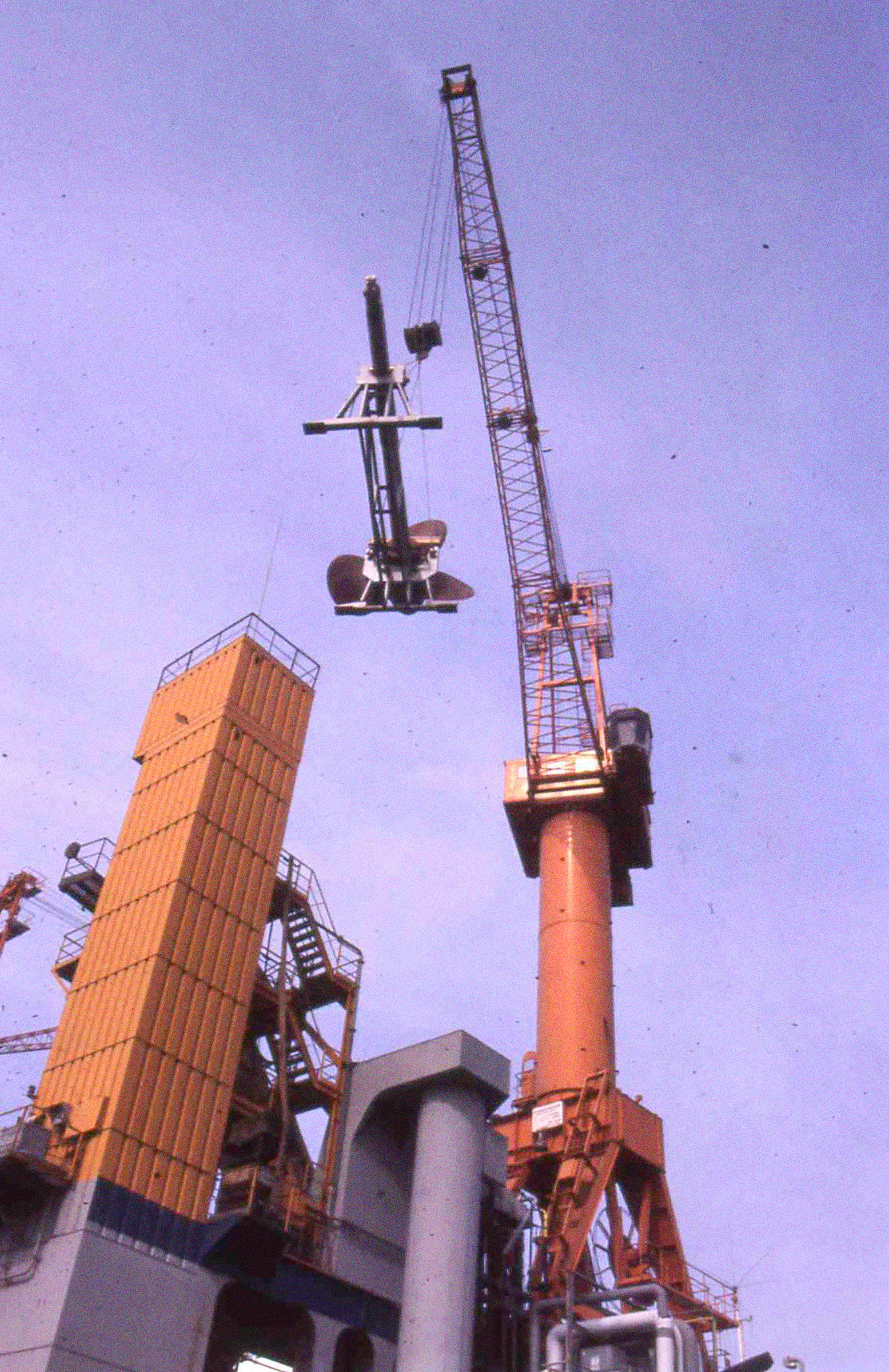 Die Propellerwelle hängt an einem Kran. Von unten fotografiert, im Hintergrund blauer Himmel.