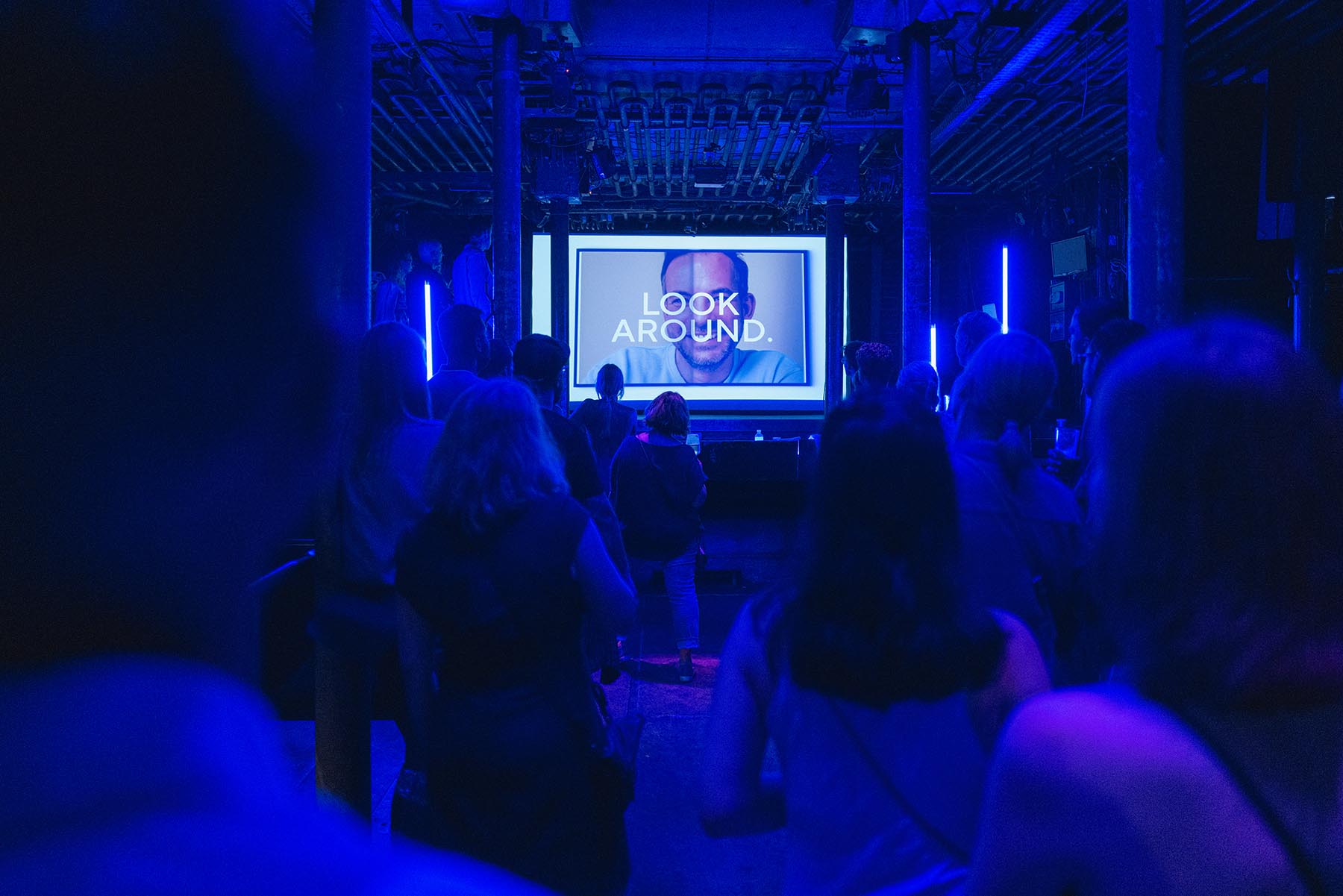 Eine Präsentation im blau beleuchteten Laderaum 4. Hier stehen Menschen, die auf eine Leinwand im Hintergrund schauen.