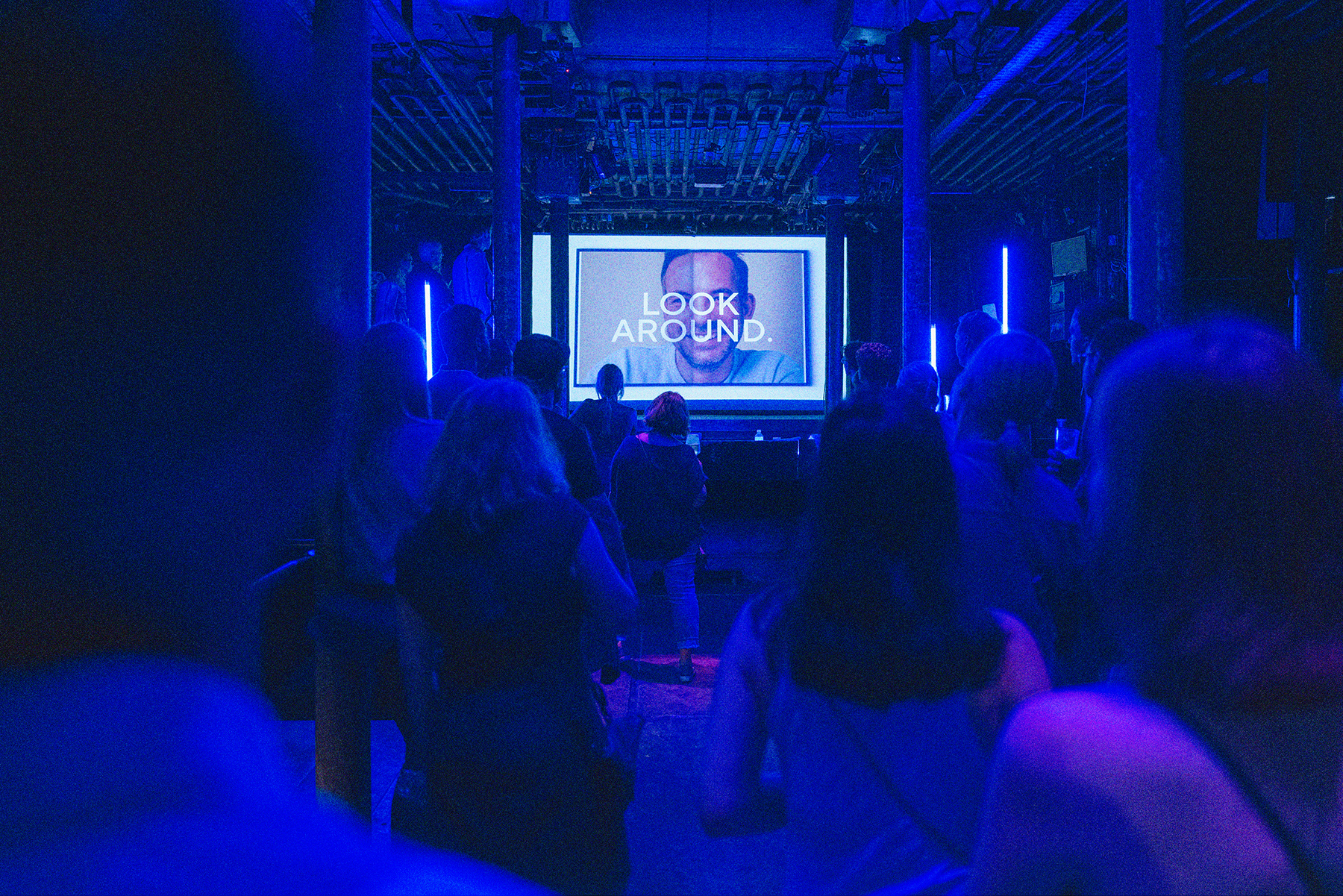 Eine Präsentation im blau beleuchteten Laderaum 4. Im Vordergrund stehen Menschen, die auf eine Leinwand im Hintergrund schauen, auf der "Look around" steht.